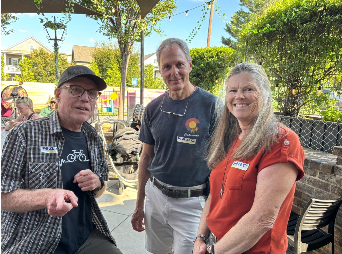 Three people smiling outside at a gathering.