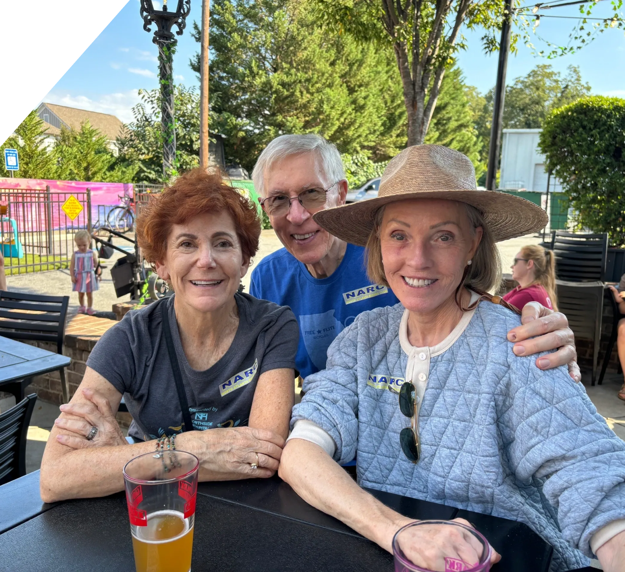Three people smiling at outdoor table.